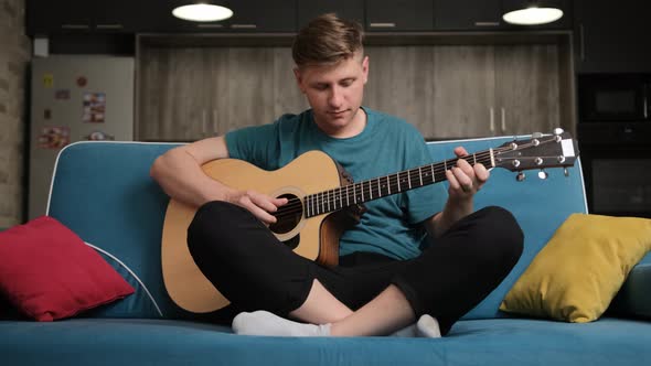 Caucasian Man Sitting on a Blue Sofa and Playing at the Guitar.