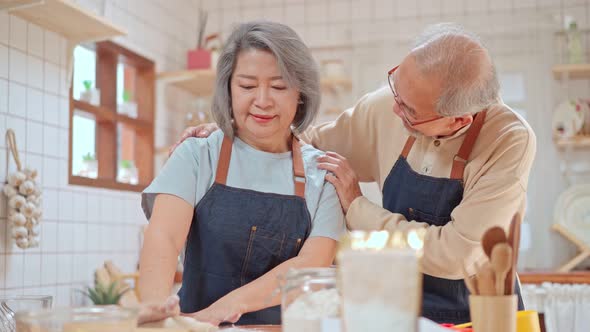 Asian Senior elderly couple cooking food with smiling face in kitchen enjoy retirement life together