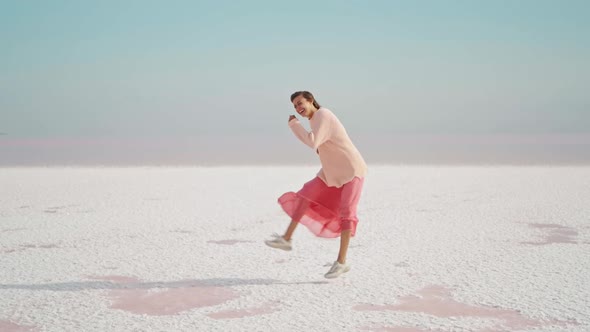 Cute Laughing Girl in Pink Oversize Sweater and Dress Funny Dancing on White Salty Desert Background