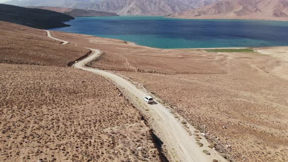 Aerial Over Off Road 4X4 Car Driving Along Gravel Trail Path Toward Lake in Arid Mountains