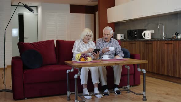 Senior Grandparents Couple Talking and Using Digital Tablet Computer at Home. Coronavirus Lockdown