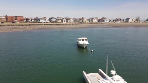 Drone circle of a weathered lobster boat moored near the shore. Other boats, coastline and building