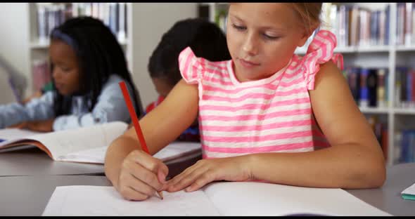 Schoolgirl drawing in book in classroom