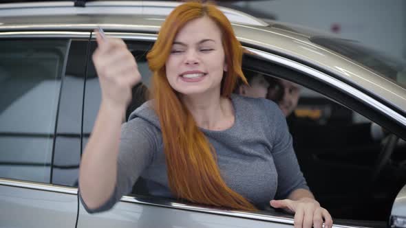 Portrait of Beautiful Redhead Caucasian Woman Holding Car Keys and Making Victory Gesture