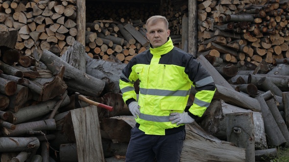 Lumberjack in Reflective Jacket. Man Woodcutter Hold Small Axe, Show Thumb Up. Sawn Logs, Firewood