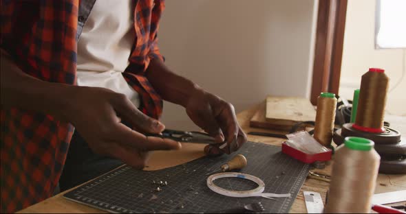 Close up of hands of african american craftsman using tools in leather workshop