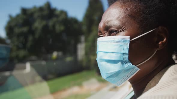 Senior african american woman wearing face mask standing by window in slow motion