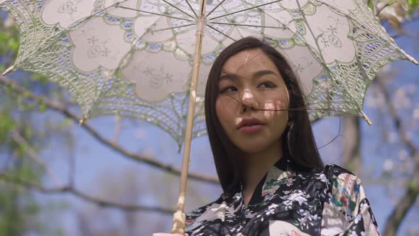 Portrait of Confident Young Asian Woman Standing in Summer Park with Sun Umbrella Looking Around