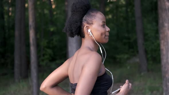 Running Black Woman in Sports Training with Headphones at Sunset on the Nature. Healthy Lifestyle