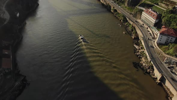 River with Motorboat Sailing Past Asphalt Road with Cars