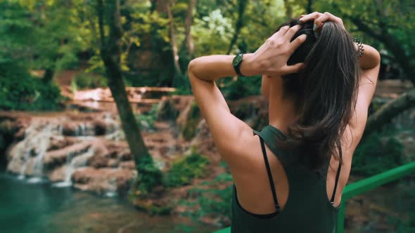 Fit Woman Fixing Her Hair While Enjoying Sunny Day in the Forest, Watching Forest Waterfalls