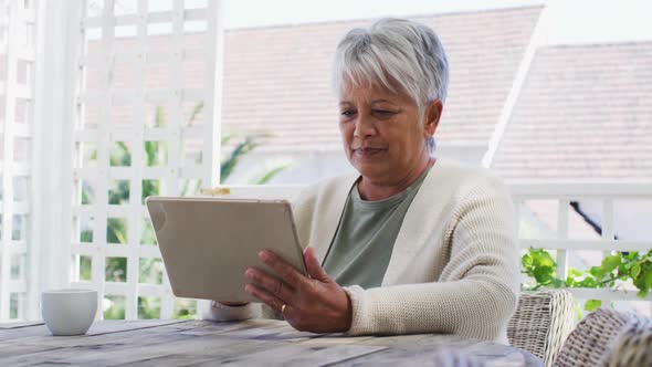 Senior mixed race woman having coffee using tablet in garden