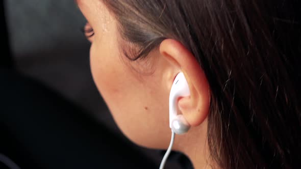 A Young Woman Puts Earpieces Into Ears and Listens To Music - Closeup