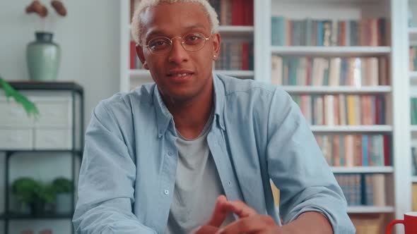 Camera View Young African American Man with Glasses Sits at Office Table