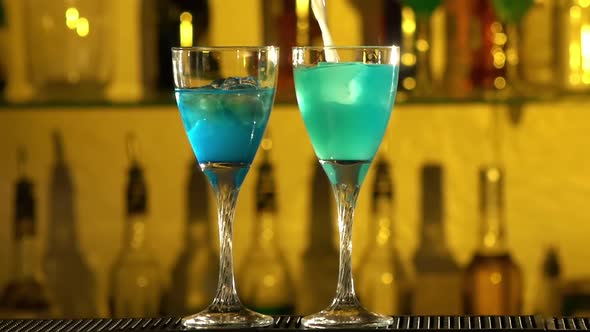 Barman Puts Cubes of Ice Into a Glass, Pouring Three Different Alcohol Liquids, Turquoise