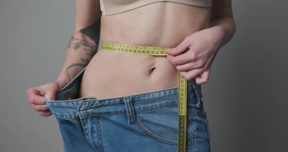 Woman with Big Jeans Controlling Her Measures Using a Tape