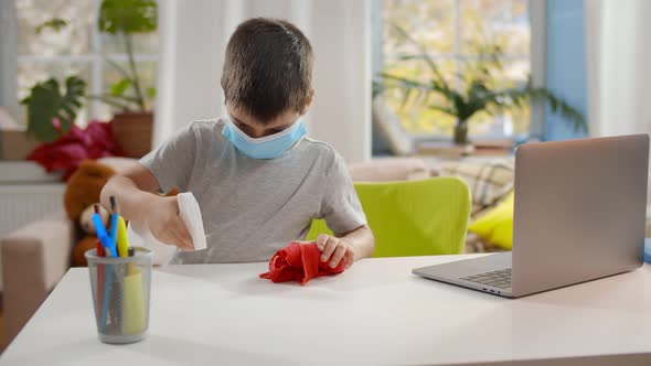 Little Boy in Safety Mask Cleaning Table with Cloth and Detergent at Home