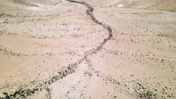 Drone descending crane shot focusing on hiker in vast desert landscape. Location is the Ramon Crater