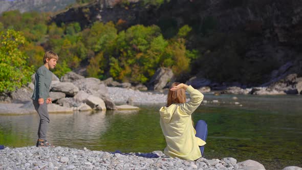 A Woman and Her Son Relax at the Riverbank Throwing Stones Into the Moracha River