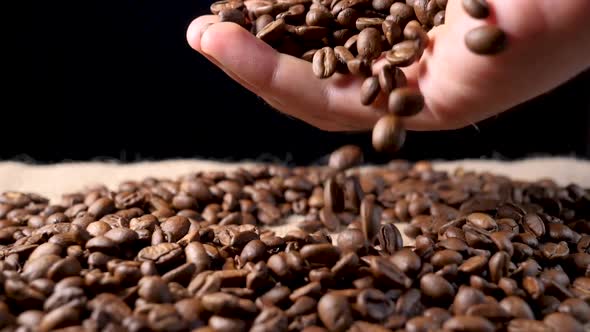 Hand mixing roasted coffee beans. Slow motion of arabica coffee seeds.