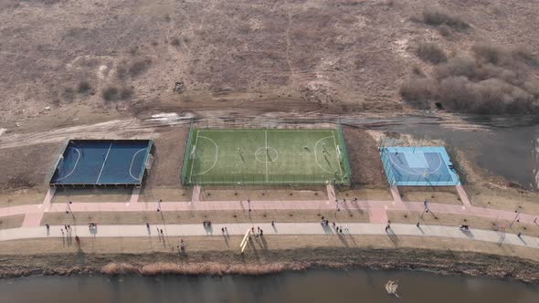 People spending holidays on fresh air, walking on promenade along river with football field