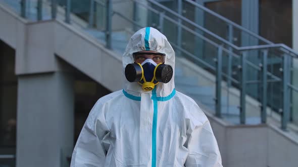 Portrait of a Young Man in a Protective Suit, Respirator, Gloves and Safety Glasses Looks Into the