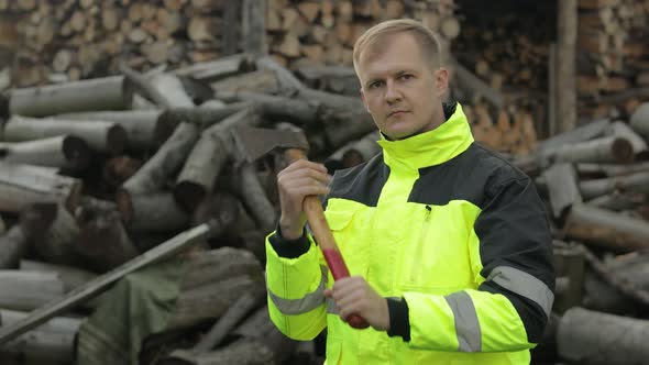 Lumberjack in Reflective Jacket. Man Woodcutter with Small Axe. Sawn Logs, Firewood Background