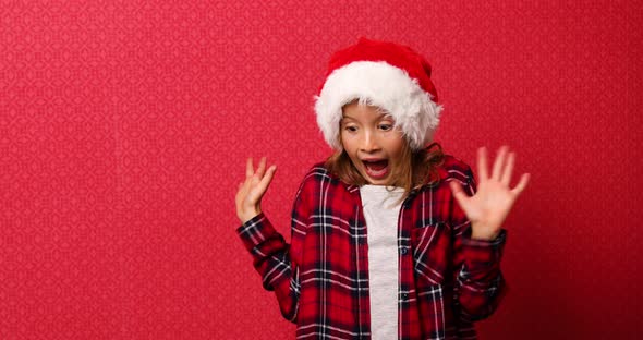 Funny little girl in santa hat, fall Christmas gift boxes arise in hand isolated on red background,