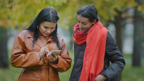 Two Hispanic Girls Stand in Autumn Park Using Telephone Women Ordering Food Taxi in Mobile