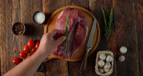 A Man's Hand Puts Rosemary on Raw Beef. 