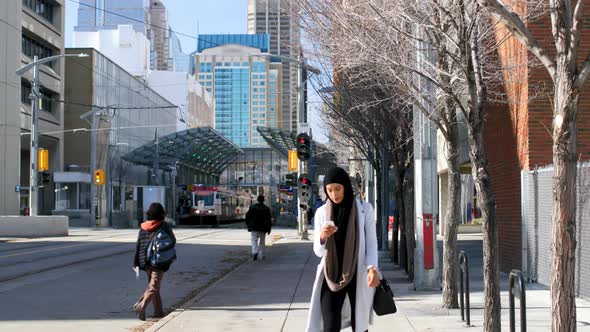 Front view of young Asian woman in hijab using mobile phone in the city 4k