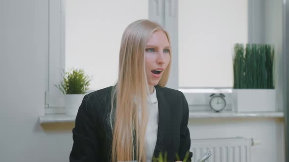 Woman Celebrating Success in Office. Elegant Blond Female Sitting at Workplace Holding in Hands