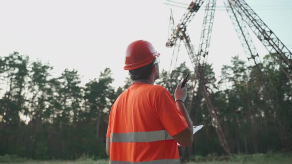 Power Plant Worker Walks and Makes Report on Walkietalkie Checking Data in Clipboard at Outdoor Work