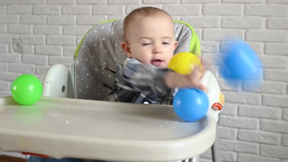 Baby Boy in a Plaid Shirt Sitting at a Children's Table Throws Multicolored Plastic Balls