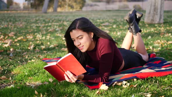 A cute young woman college student reading a book outdoors in the park before class starts in the fa