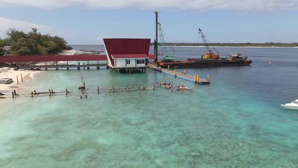 Industrial ship moored on pier surrounded by clear water with coral reef on luxury island.Aerial fli