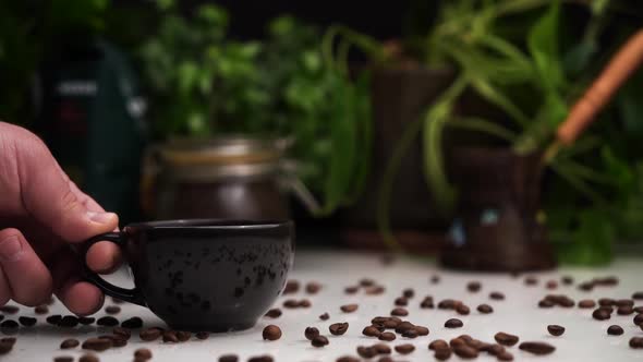 Man Hand Place Black Cup of Hot Coffee or Espresso on White Table with Coffee Beans on It.