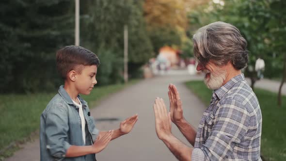 Little Boy and Grandfather Playing with Hands in a Park