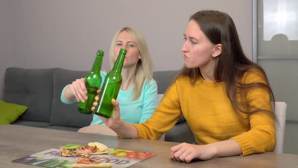Two best happy girlfriends at home in kitchen eating pizza and drinking beer.