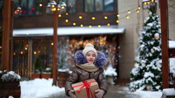 Portrait of joyful girl with a gift box for Christmas on a city street in winter with snow on a fest