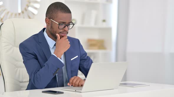 Pensive African Businessman Thinking and Working on Laptop 