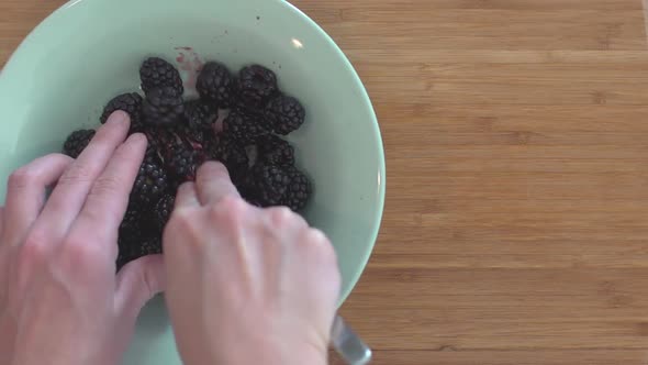 A woman squishing blackberries with a fork