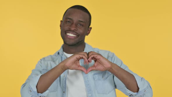 Young African Man Heart Sign By Hand, Yellow Background 