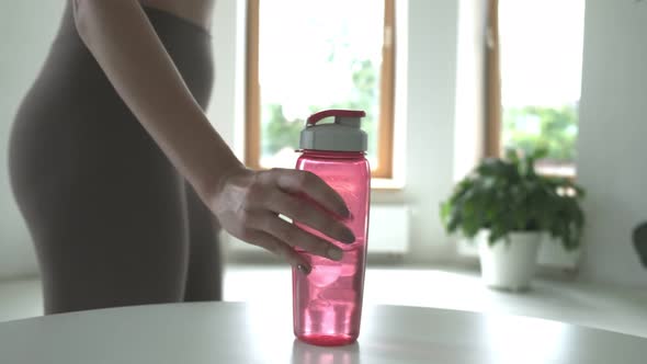 Fit Woman Putting Pink Plastic Bottle of Water on Table in Bright Room Closeup