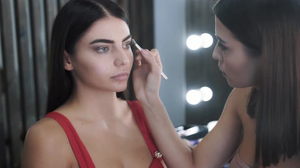 Pretty Woman Makeup Artist Applies Makeup to Young Beautiful Brunette Woman