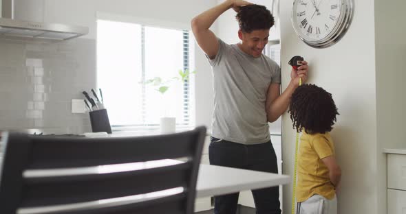 Happy biracial man and his son measure height in kitchen