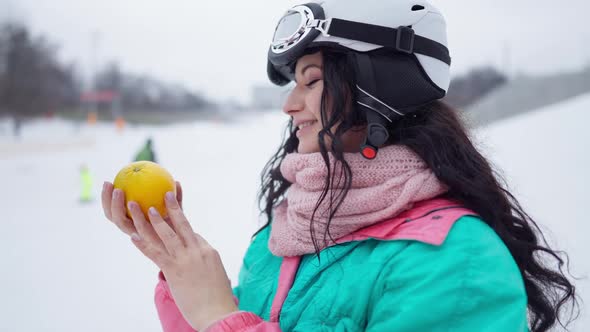 Side View of Happy Beautiful Woman Smelling Healthful Orange in Slow Motion Standing in Snowy