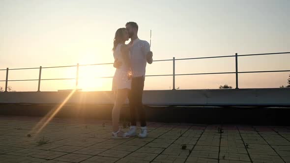 Couple on roof at sunset on summer evening during party holding sparklers