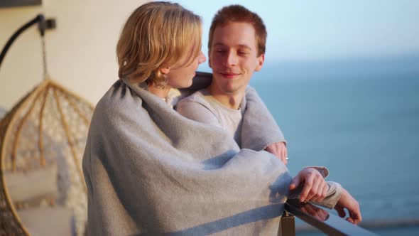 Smiling gay couple talking on the balcony under a blanket