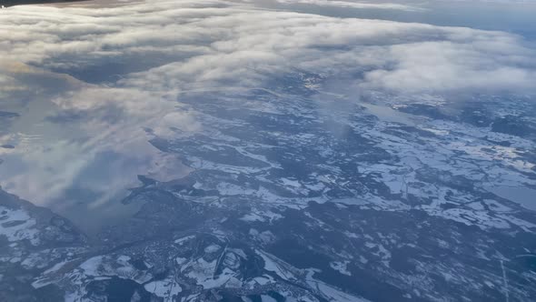 Skimming above clouds over Trondheim fjord with bright golden sun contrast with blue snowy ground an